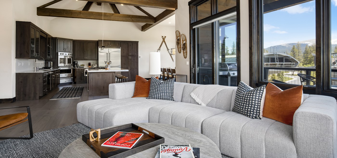 Living area with high ceilings, large grey couch with multiple armchairs, and adjourning kitchen