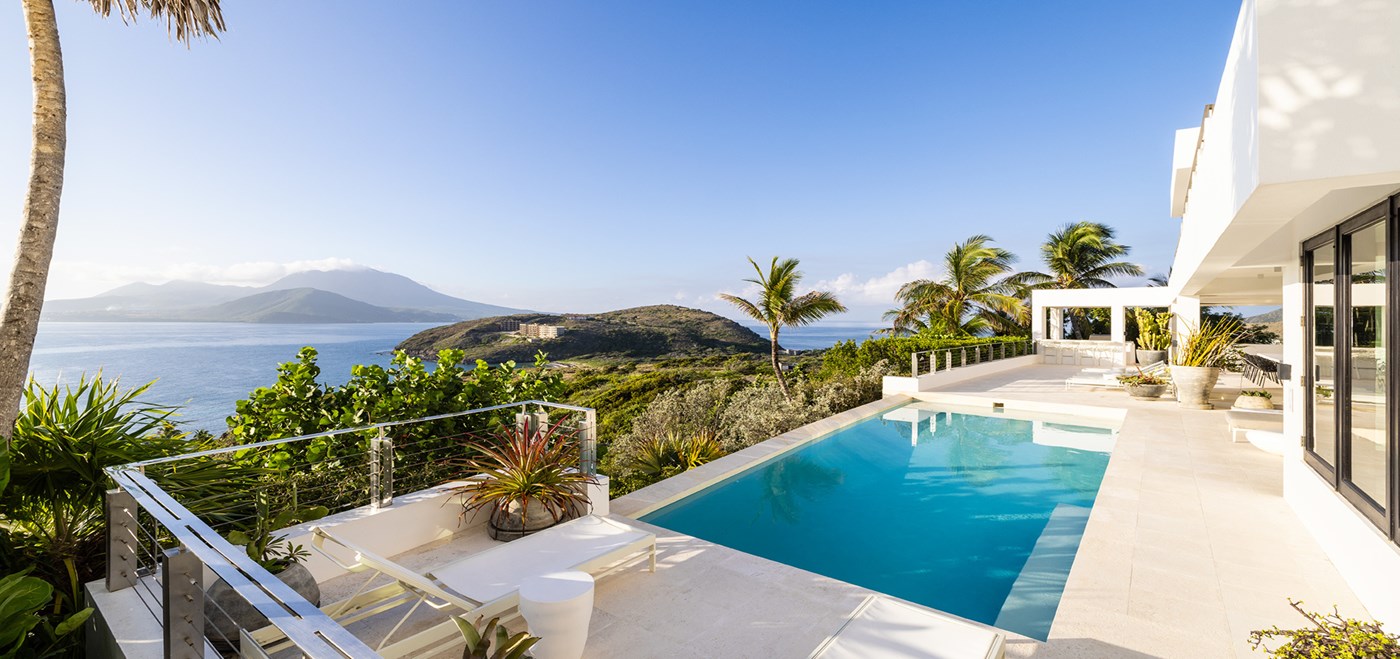 Pool with lounge chairs and surrounding forest with views of the ocean