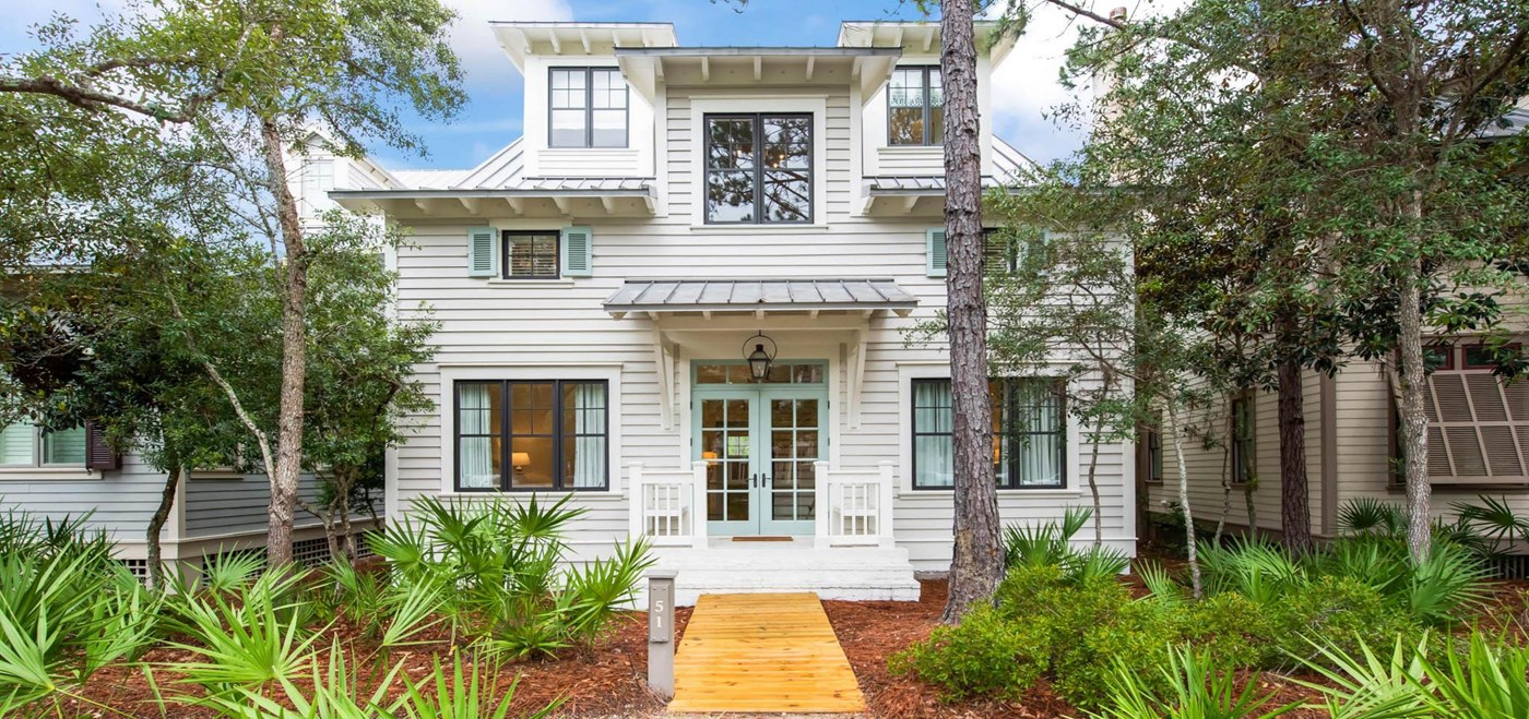 Seagrove front exterior with wooden boardwalk leading up to the seafoam colored front door with planted shrubbery planted around the front 