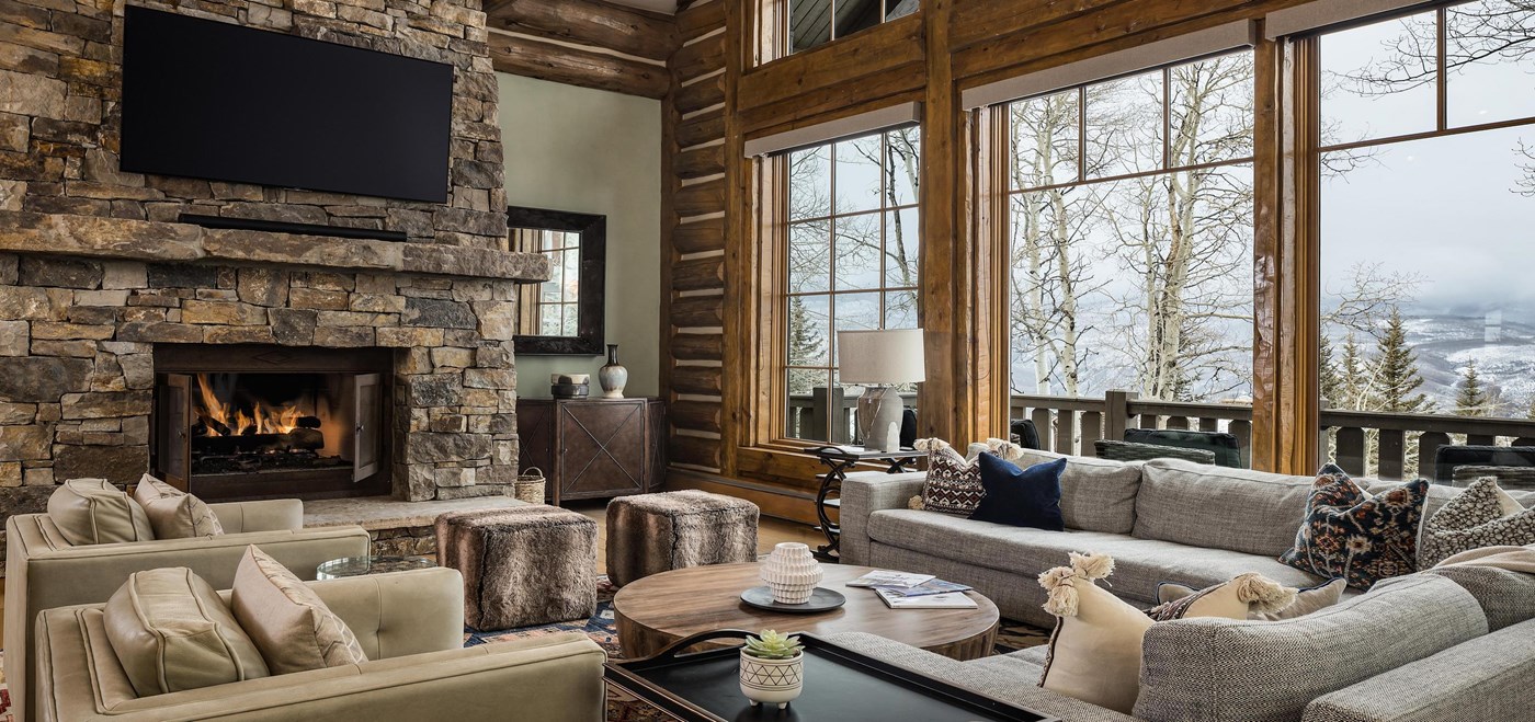 Living area with large stone fireplace with natural colored furniture arranged in front of it with large windows with wintery views